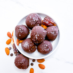 Chocolate covered date balls sitting on a small white plate.