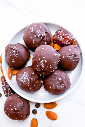Chocolate covered date balls sitting on a small white plate.