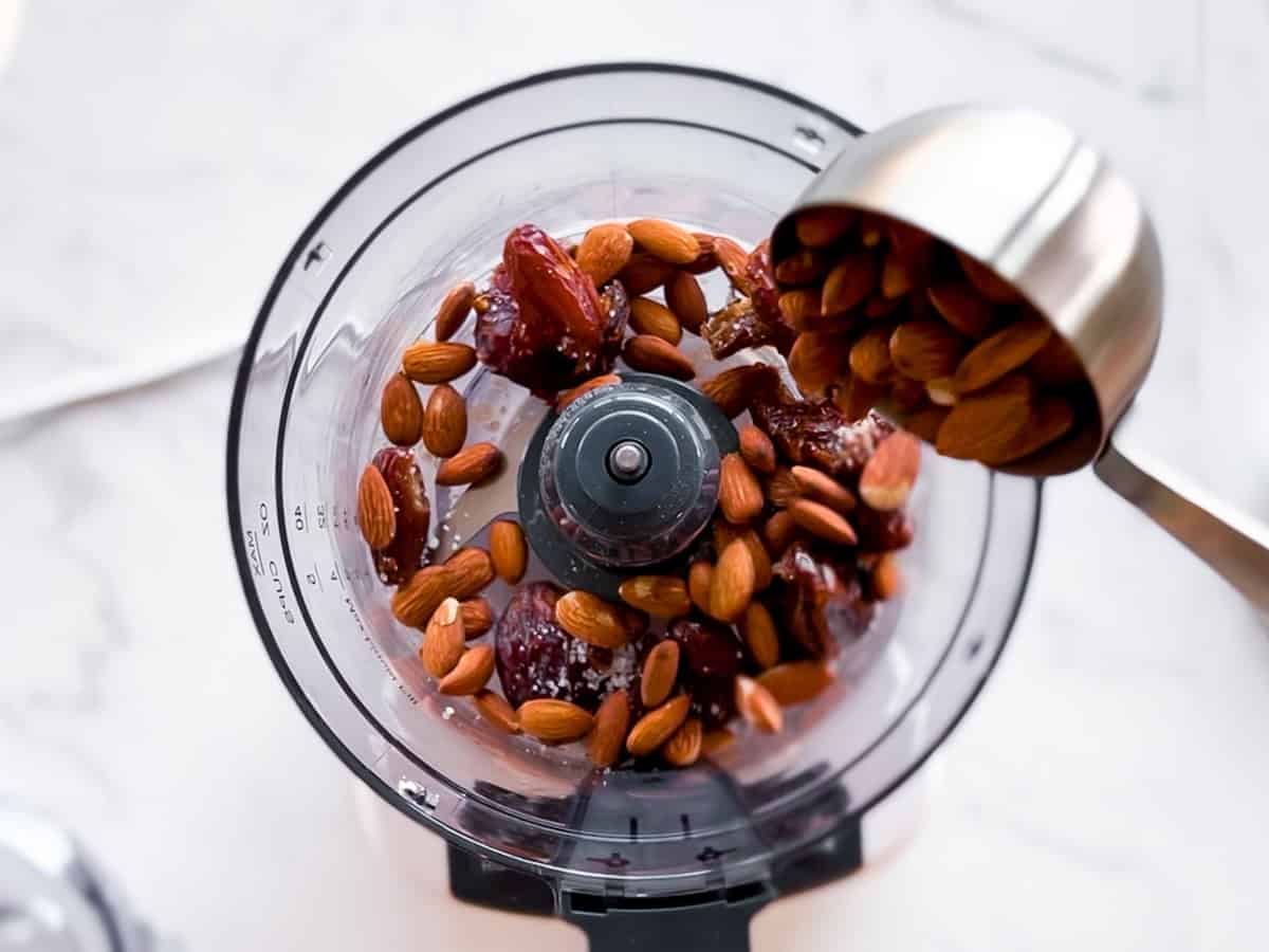 Almonds and dates being added to a food processor.