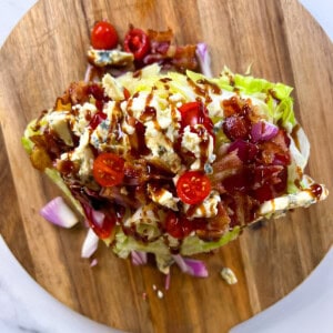 Finished wedge salad with toppings on a round wooden cutting board.