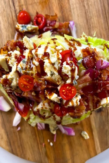 Finished wedge salad with toppings on a round wooden cutting board.