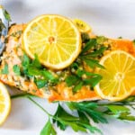 Mediterranean salmon on a white plate garnished with lemon slices and parsley.