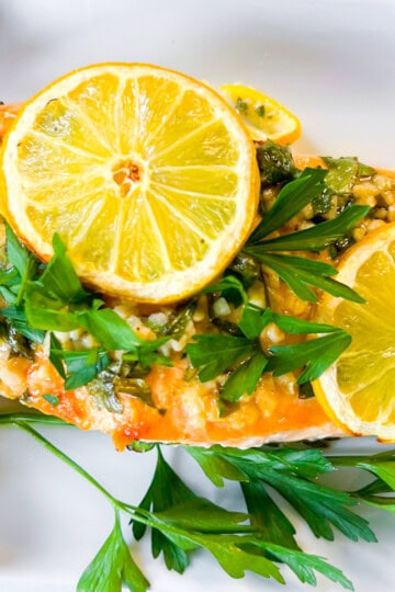 Salmon on a white plate garnished with lemon slices and parsley.