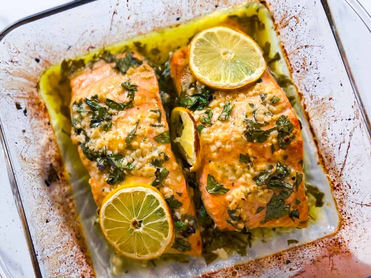 Fully cooked Mediterranean salmon in a baking dish with lemon slices and parsley on top.