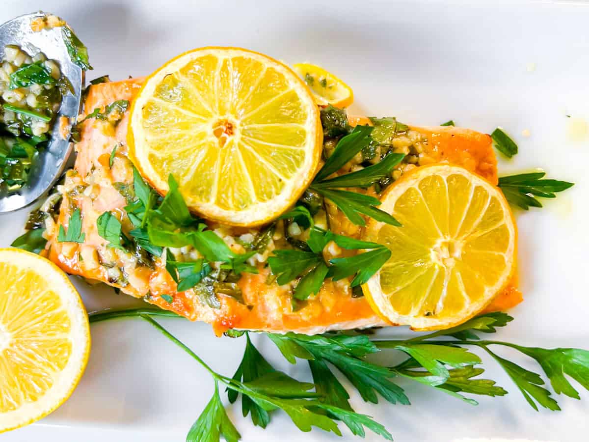 Mediterranean salmon on a white plate garnished with lemon slices and parsley.