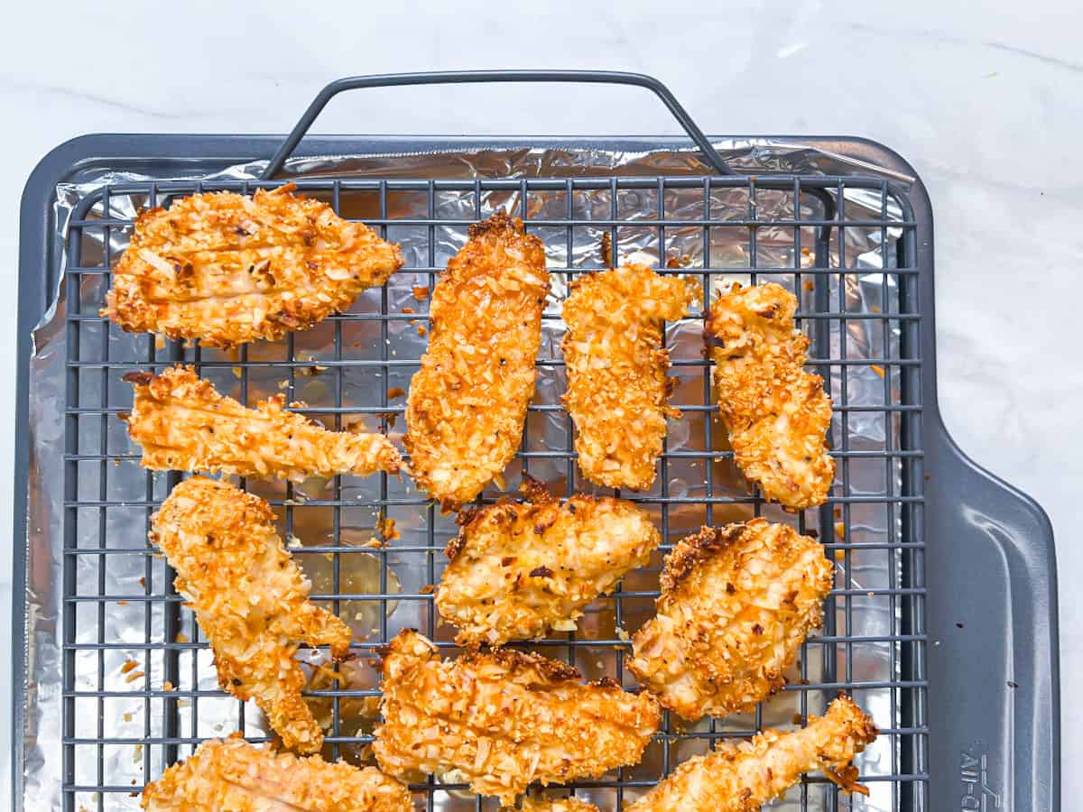 Fully baked and browned coconut breaded chicken on a baking rack.