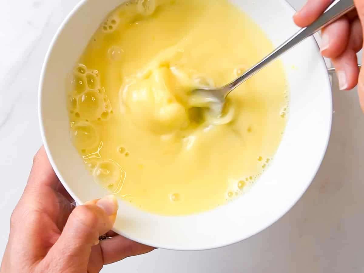 egg, coconut milk, lime, and honey being whisked together in a bowl.