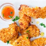 Coconut crusted chicken finished on a white plate with a dipping sauce.