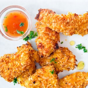 Coconut crusted chicken finished on a white plate with a dipping sauce.