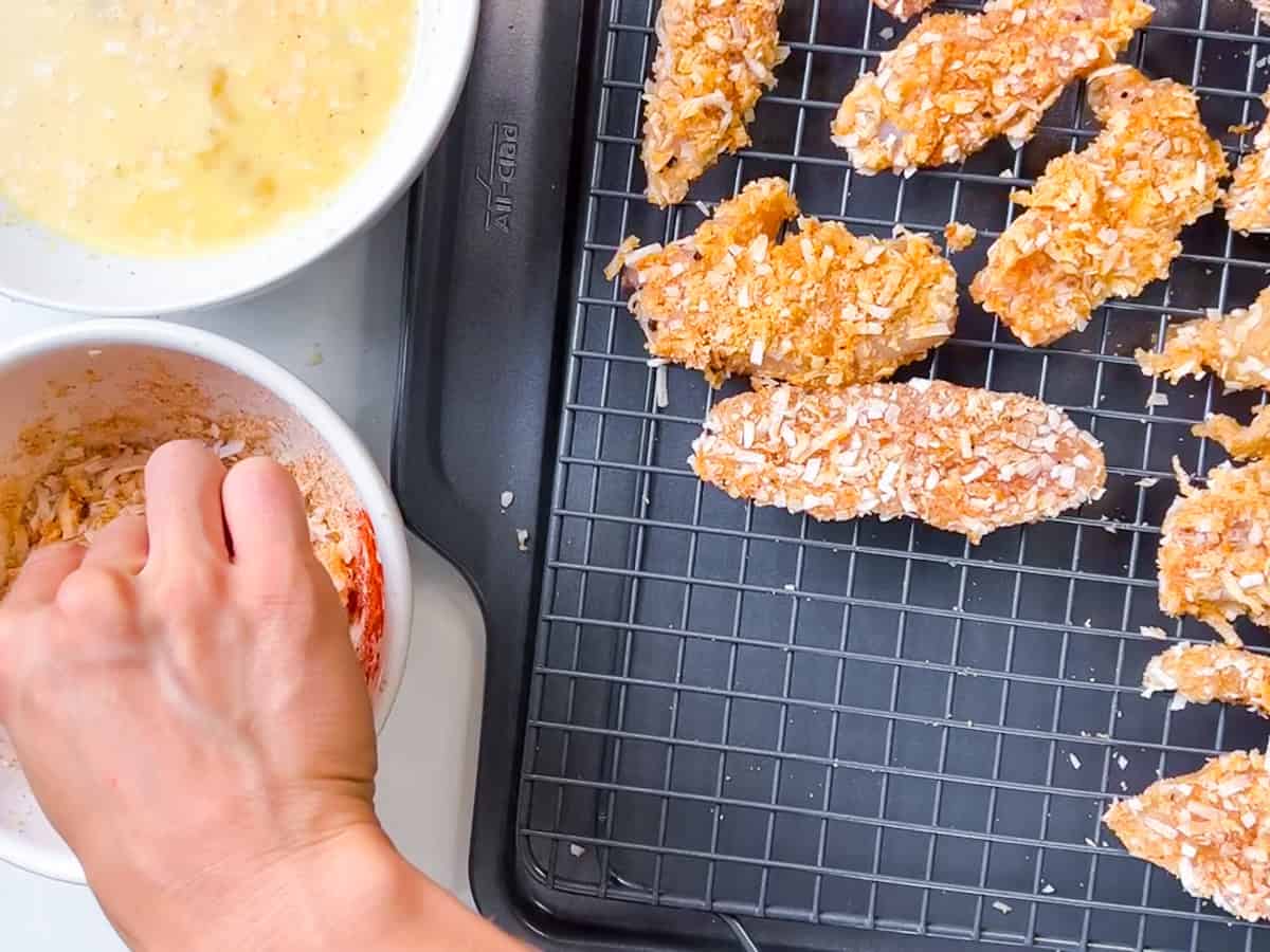 Chicken tenders being dipped at each breading station.
