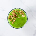 Green smoothie in a cup with granola sprinkled on top.