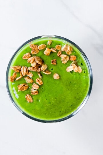 Green smoothie in a cup with granola sprinkled on top.