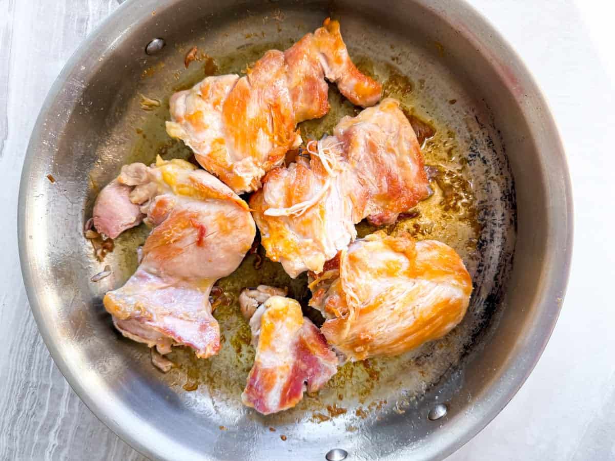Chicken cooking in a stainless steel skillet.
