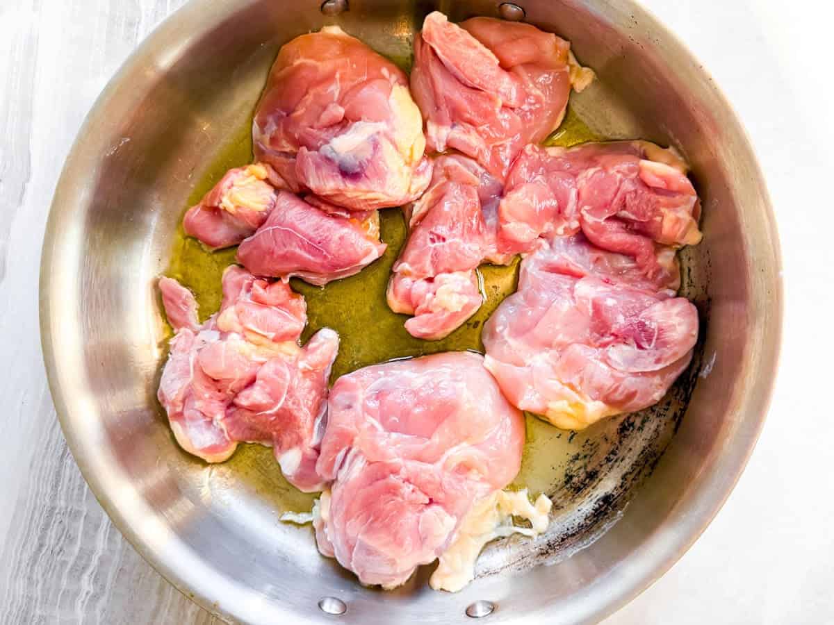 Raw chicken in a stainless steel skillet with oil.