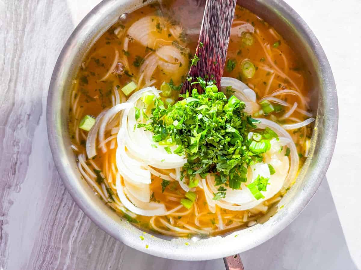 Onion and the cilantro and green onions being added to the soup broth.