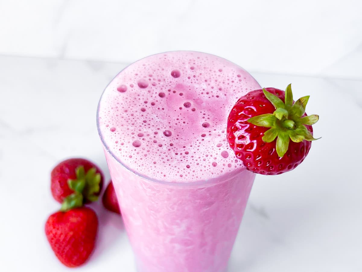 Finished strawberry protein shake in a tall glass garnished with a strawberry.