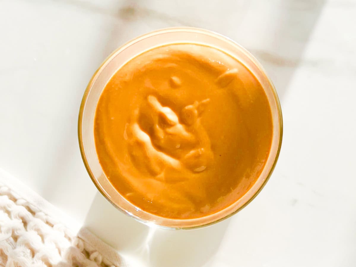 Cinnamon peanut butter in a glass jar on a marble counter.