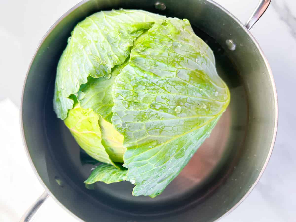 Cabbage head boiling in a pot of water.