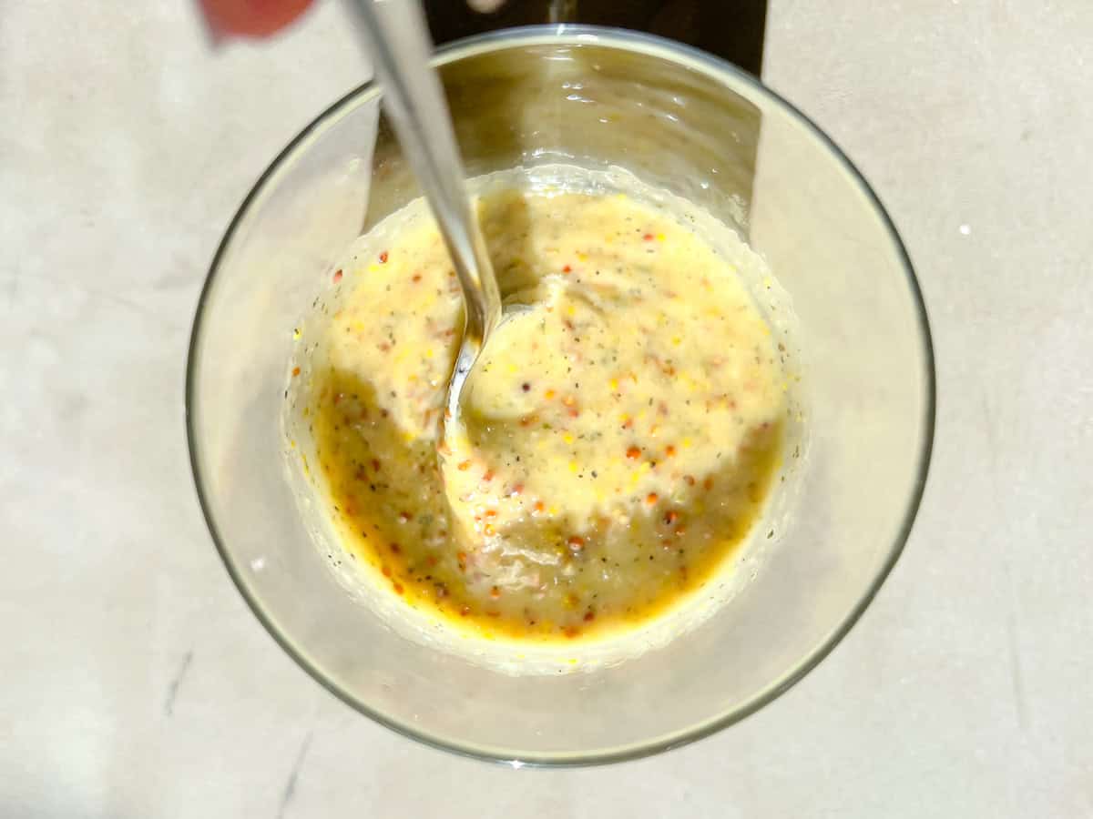 Honey mustard sauce in a clear jar being mixed.