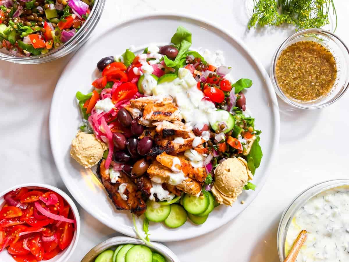 Mediterranean style bowl on a with ingredients in bowls around the plate.