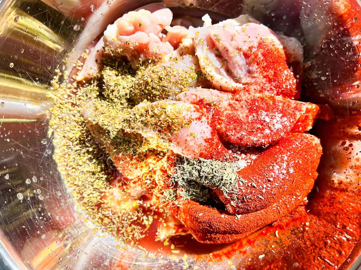 Raw chicken for the cava bowls in a stainless steel bowl with paprika, garlic, & other spices.