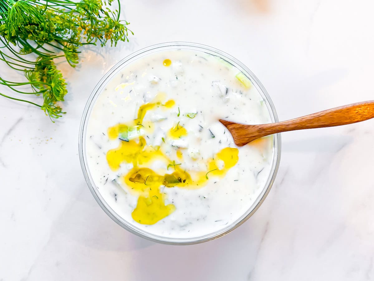 Tzatziki in a bowl with a wooden spoon and dill around it.