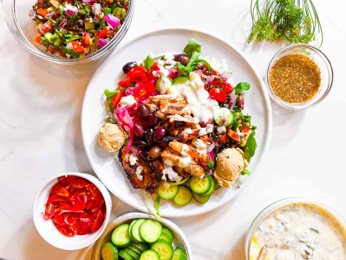 Cava style bowl with hummus, cucumbers, tabbouleh, and tzatziki on a white plate.