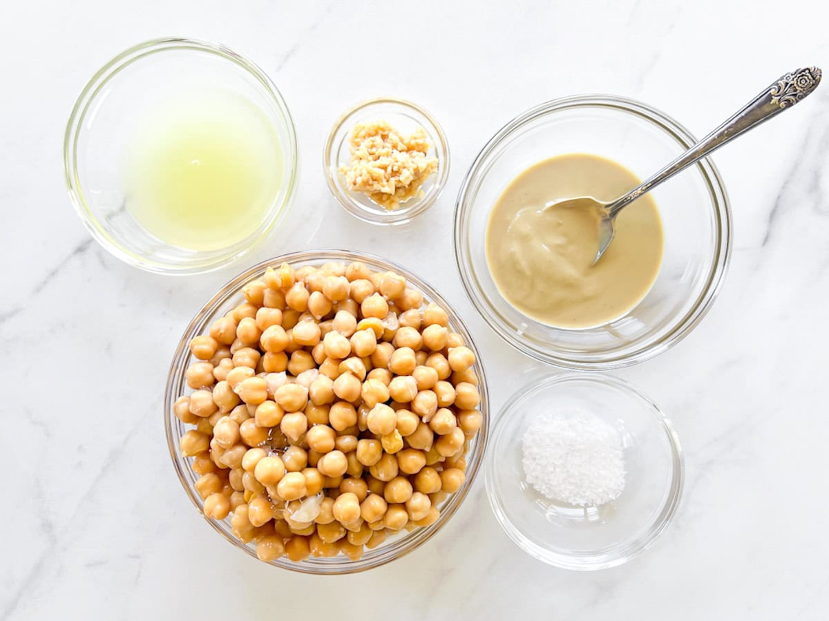 Hummus ingredients; lemon juice, chickpeas, tahini, garlic, and salt in small clear bowls.