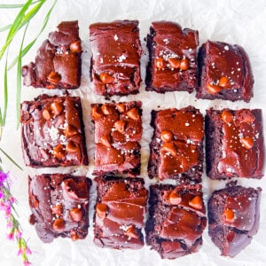Gluten free brownies cut into pieces on white parchment paper.