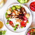 Cava style bowl with hummus, tzatziki, lentil tabbouleh, tomatoes, and pickled onions on a white plate.