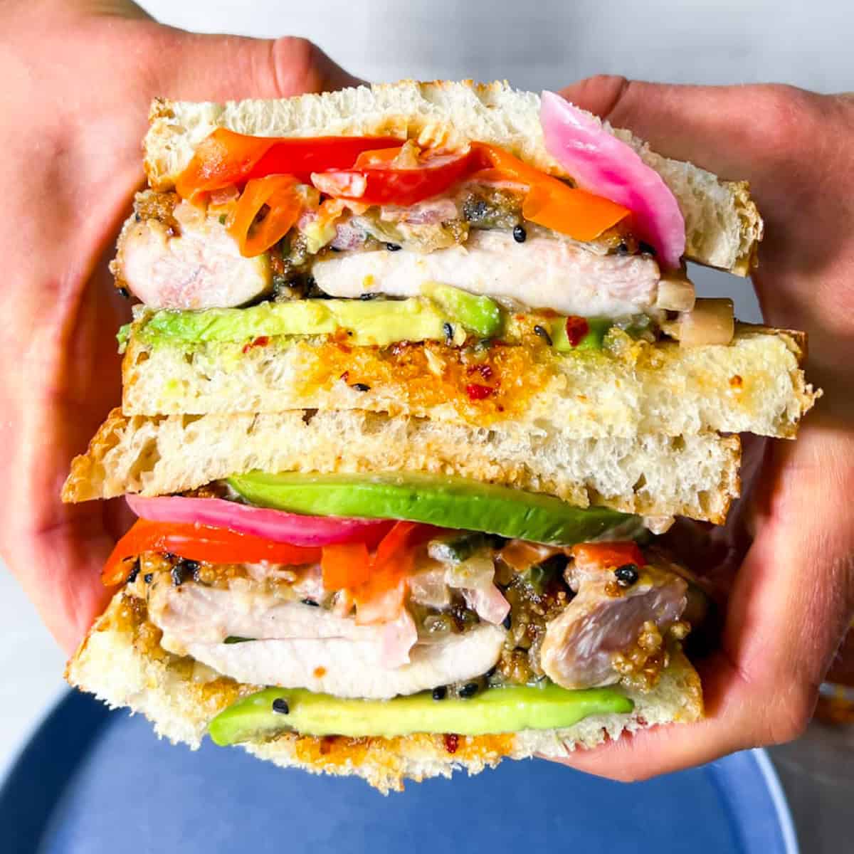 Chicken Katsu Sandwich with veggies and avocado being held.
