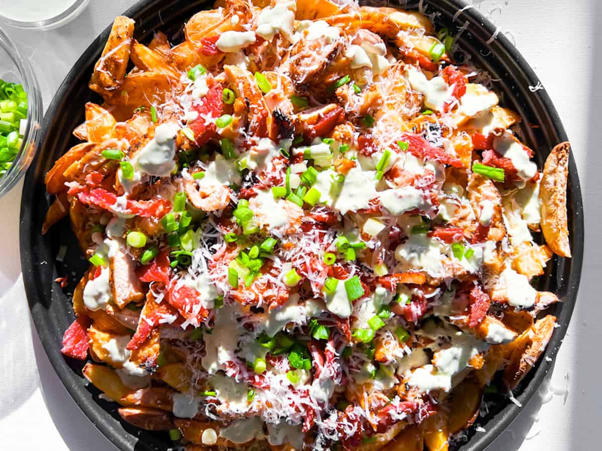 Loaded french fries on a large platter with all of the toppings.