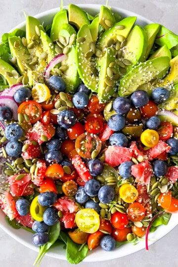 Arugula and spinach salad with avocado, vegetables, and fruit.
