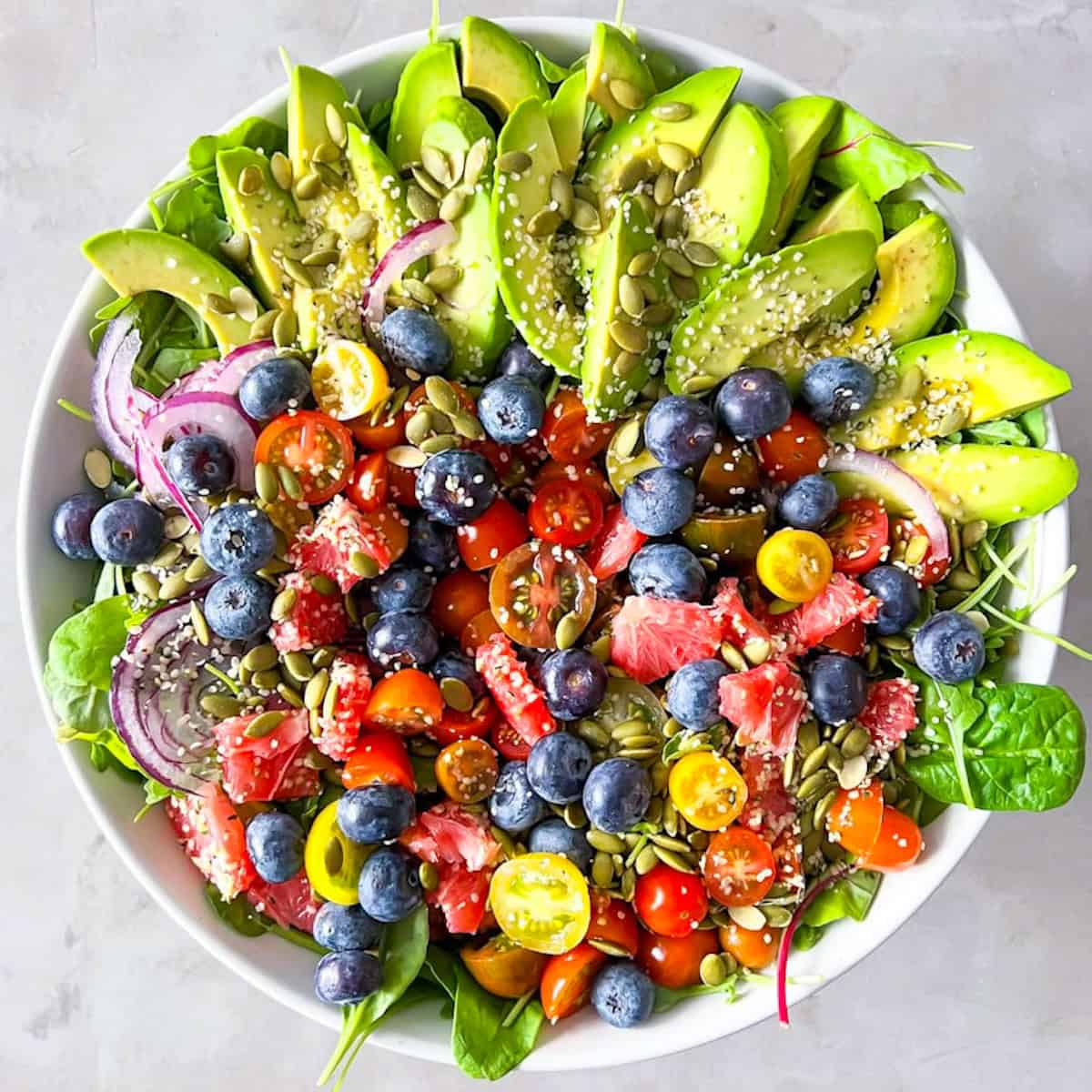 Arugula and spinach salad with avocado, vegetables, and fruit.