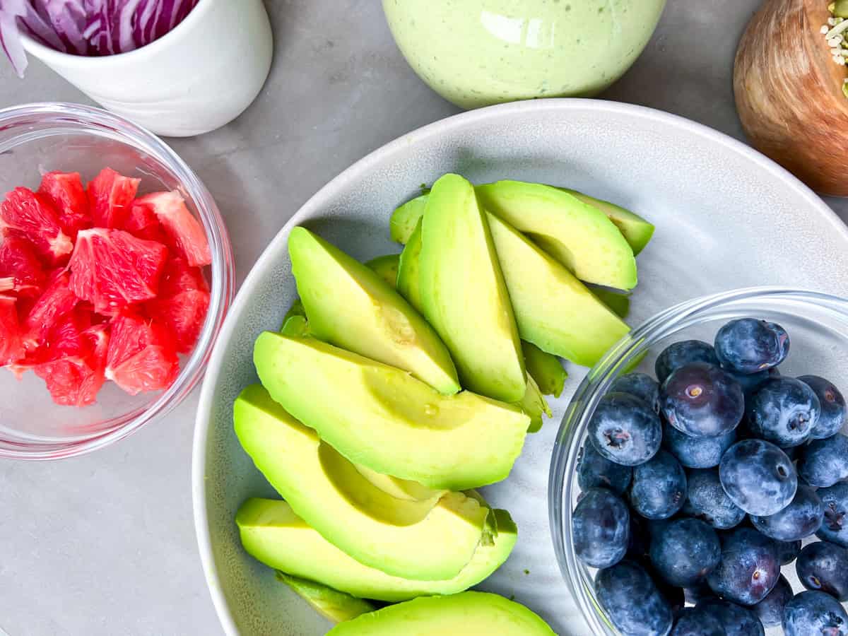 Sliced avocado on a plate with a small bowl of blueberries next to it.