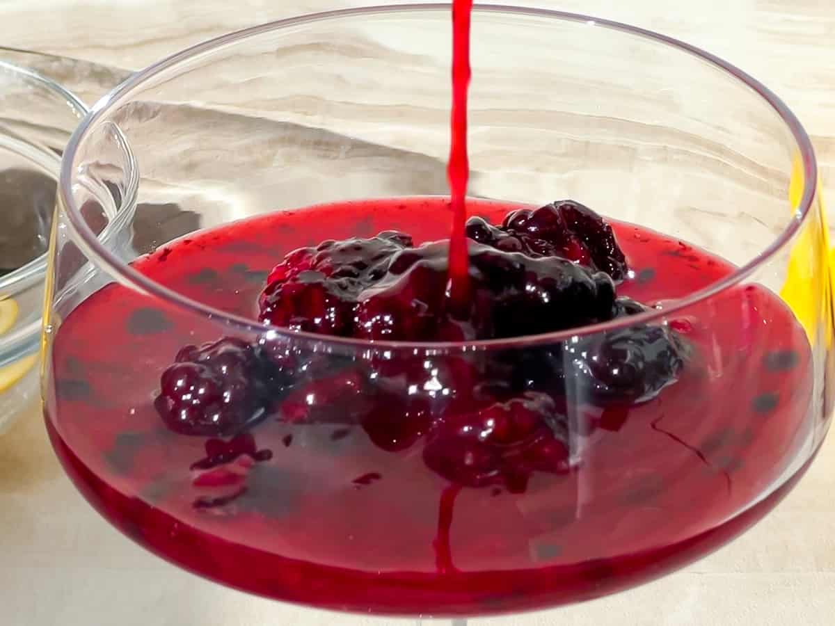 Blackberry syrup being poured into a cocktail glass.