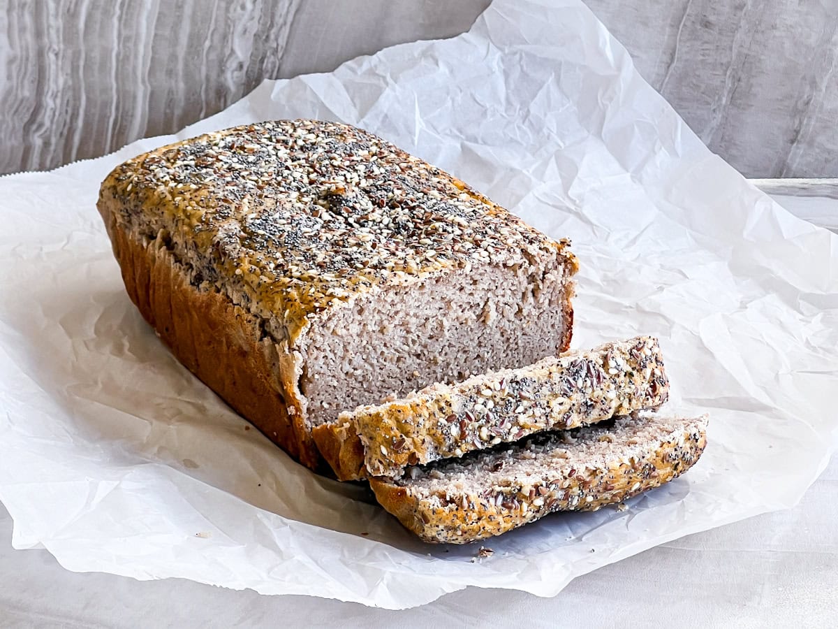 Loaf of buckwheat bread sitting on parchment paper and sliced.