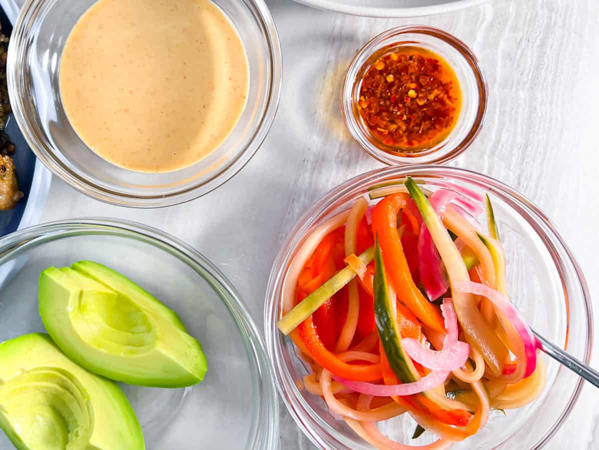Pickled veggies, avocado, spicy mayo, and chili crisp in bowls.