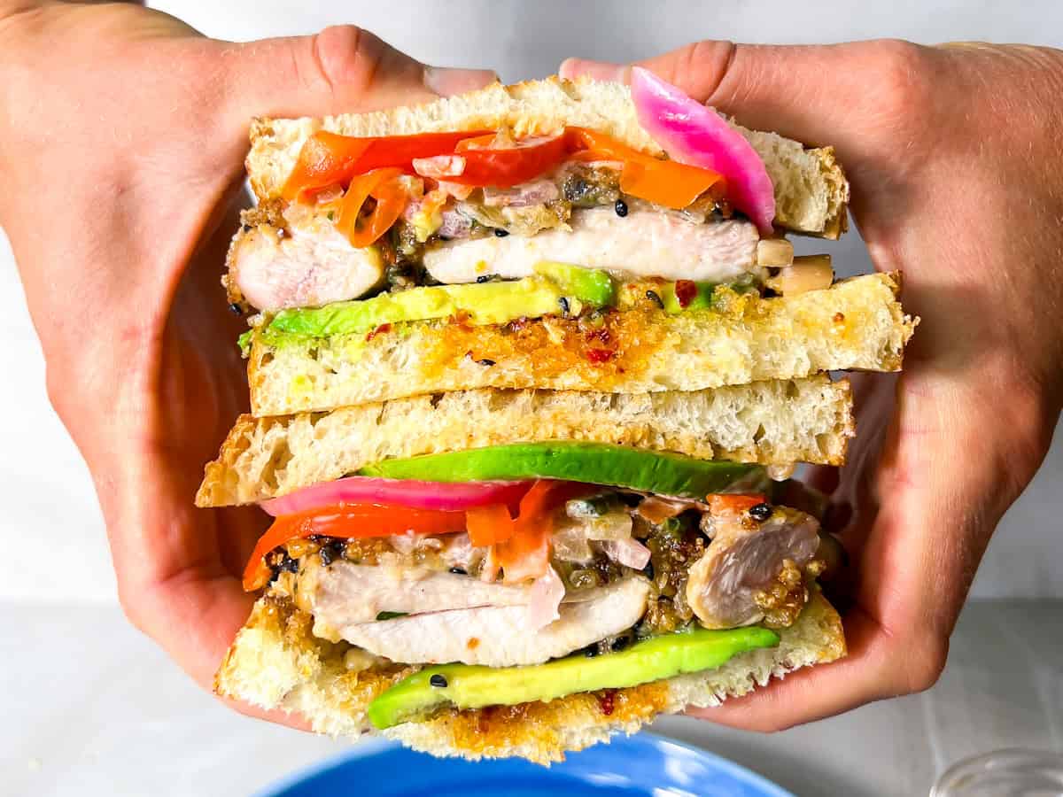 Hands holding a cut chicken katsu sandwich.