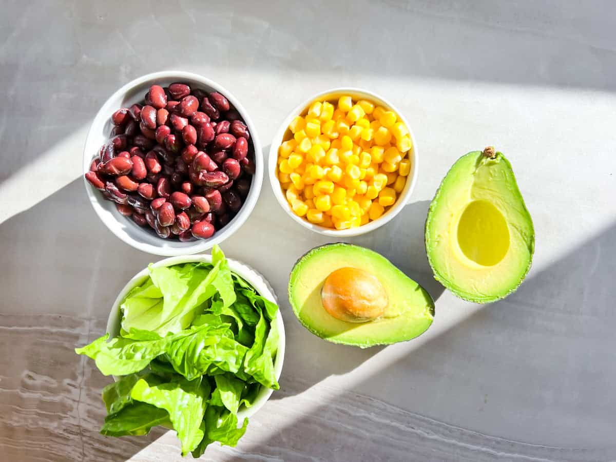 Corn and beans rinsed and drained in bowls next to a halved avocado.