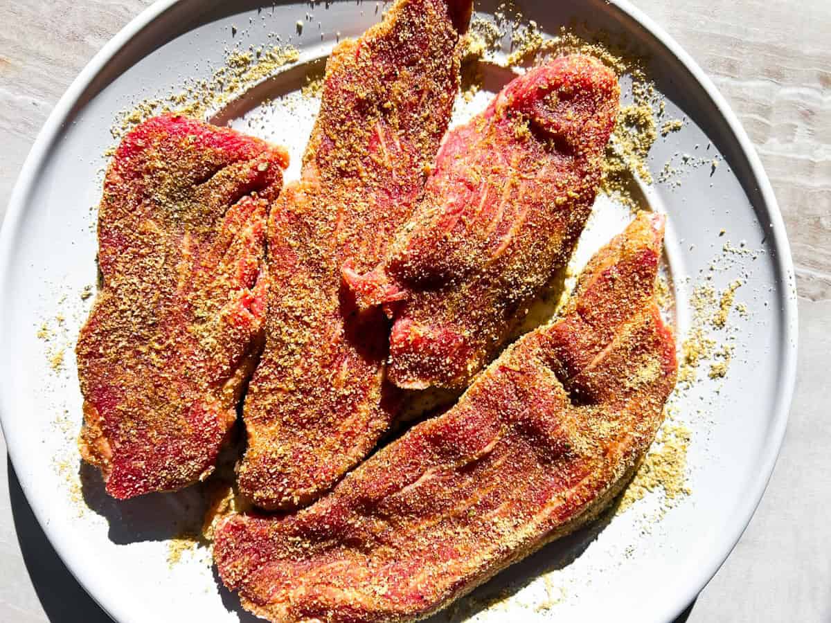 Uncooked steak seasoned and on a plate.