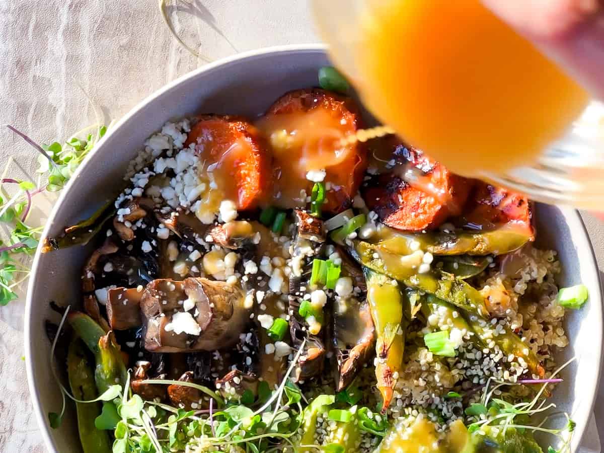 Ancient grain bowls assembled with honey miso dressing being poured on top.