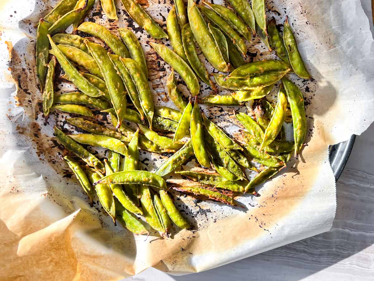 Broiled snap peas on parchment paper.