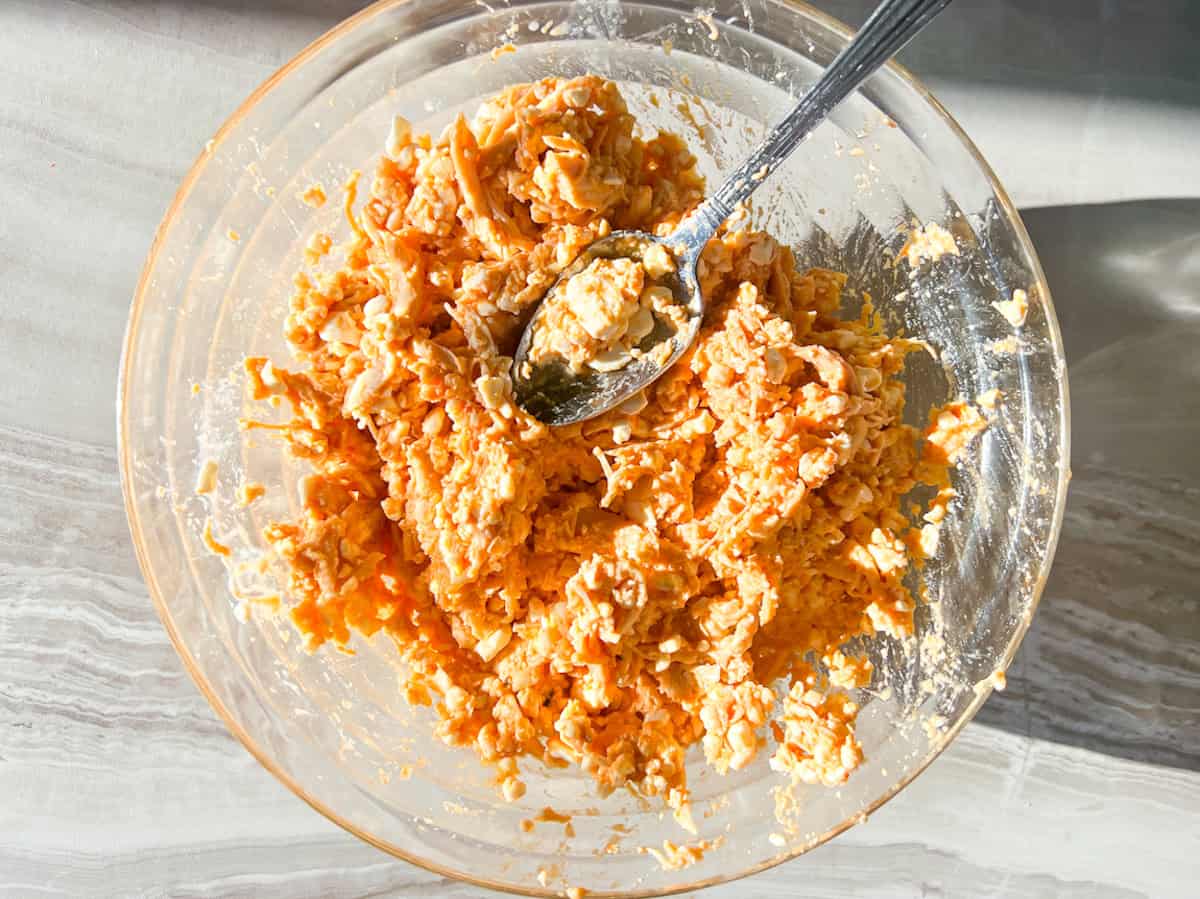 Shredded chicken mixed with cottage cheese, feta, and spices in a clear bowl.