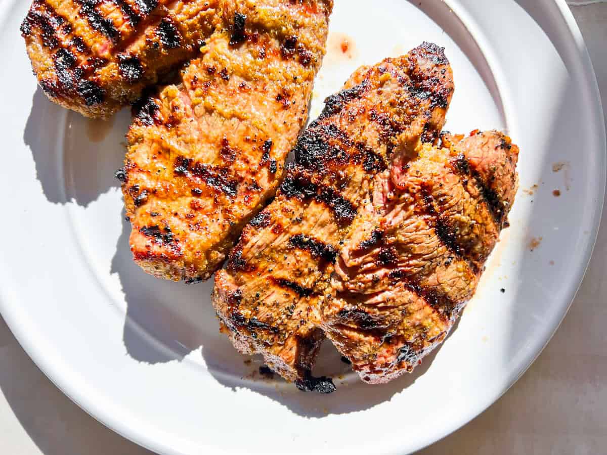 Fully cooked steaks on a white plate.