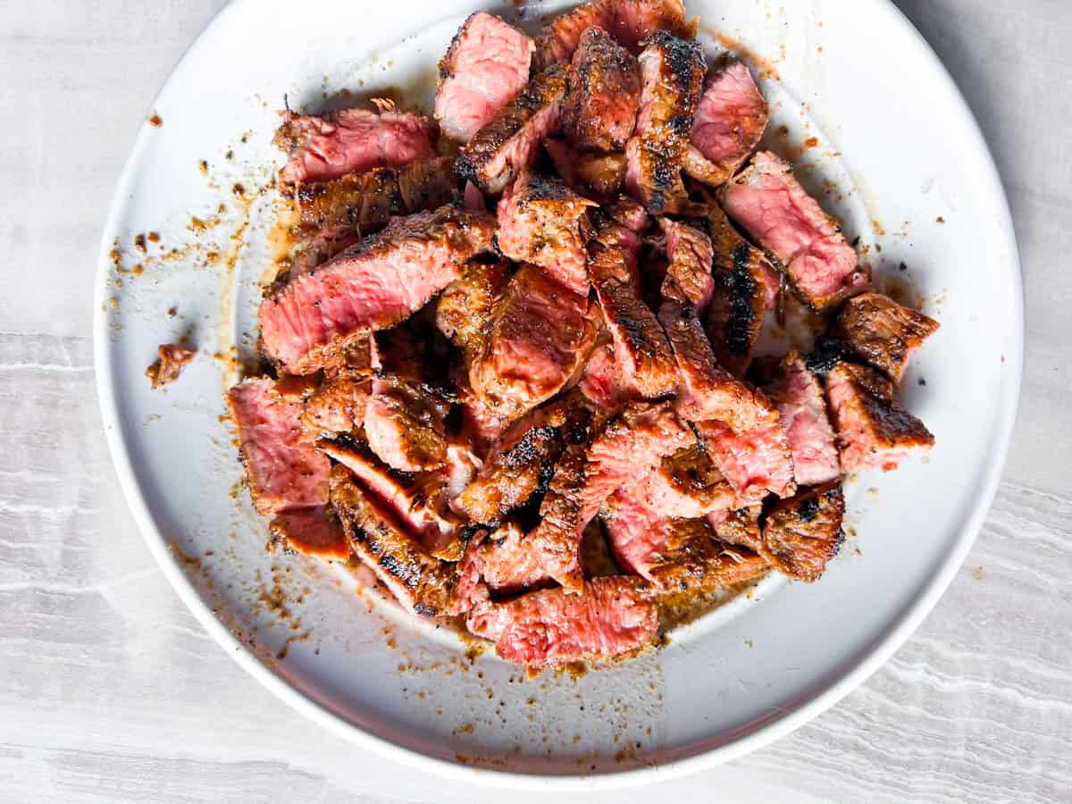 Sliced steak strips on a white plate.