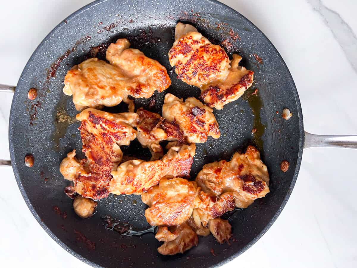 Browned chicken thighs cooking on a skillet.