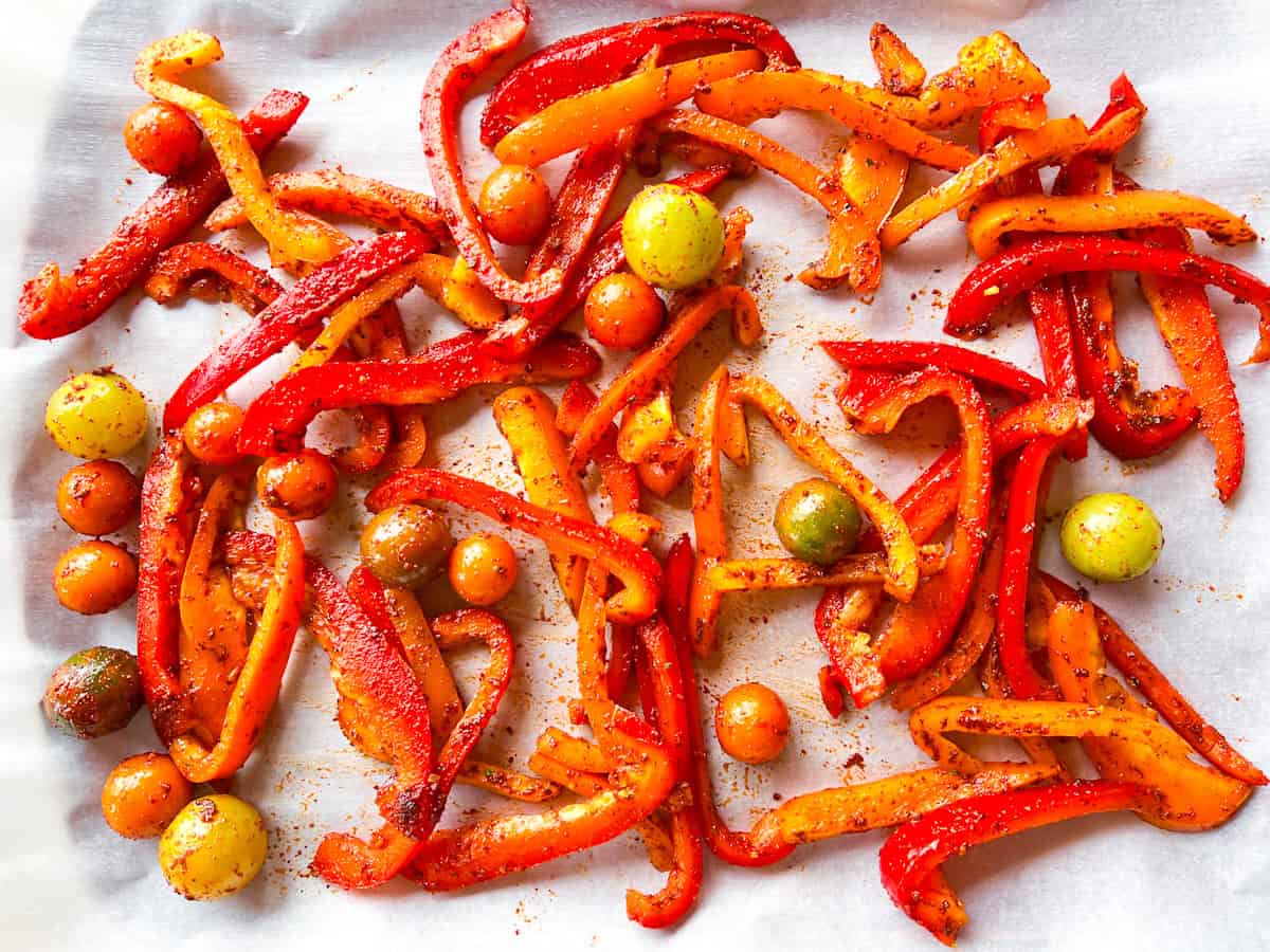 Seasoned peppers and tomatoes on a sheet pan.