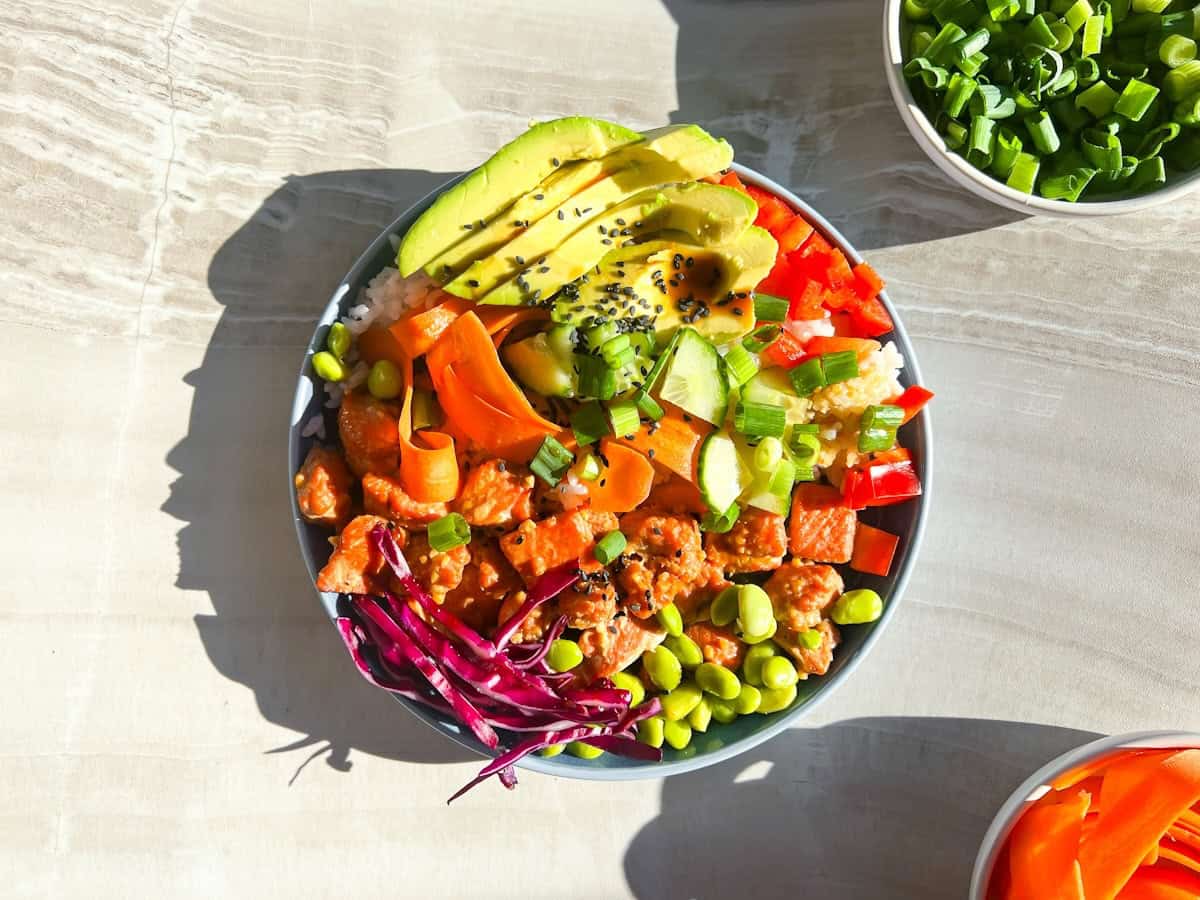 Salmon poke bowls in a blue bowl with ingredient bowls around it.
