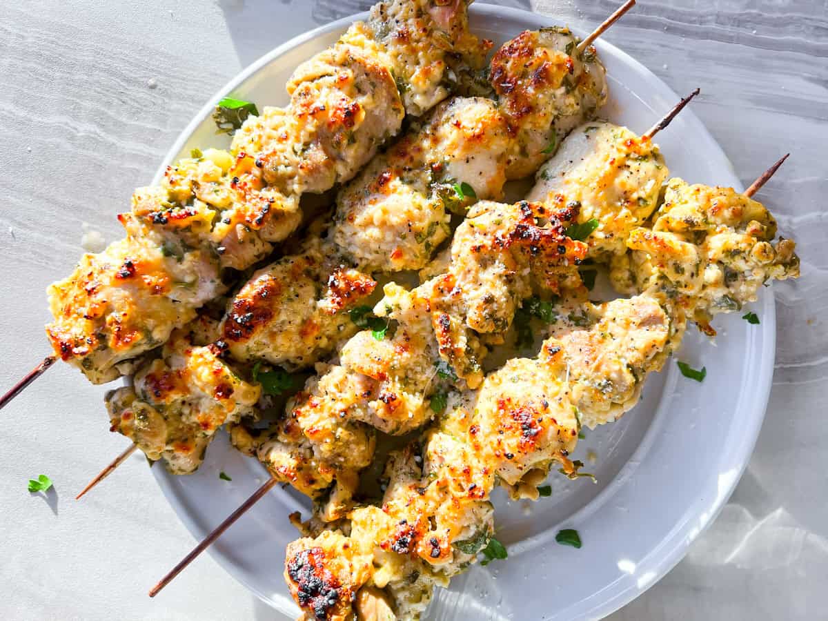 4 finished garlic parmesan chicken skewers on a white plate.